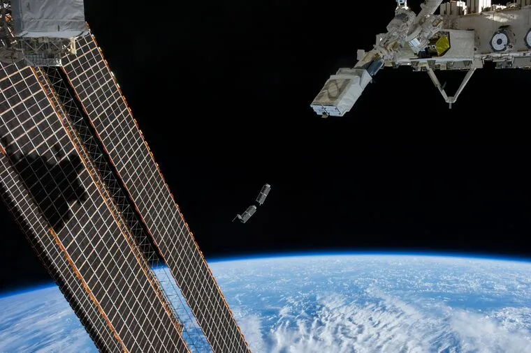 CubeSats deploying from the NanoRacks launcher on the International Space Station, the cloud-covered Earth below