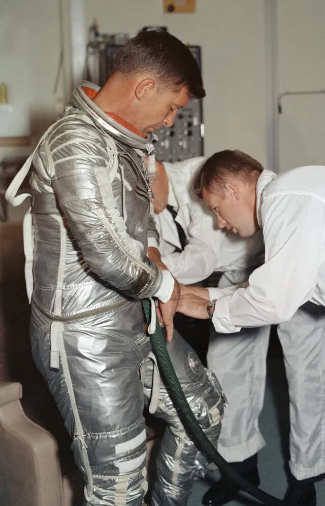 Astronaut Walter Schirra in a silver Mercury pressure suit being suited up by technicians before the MA-8 flight