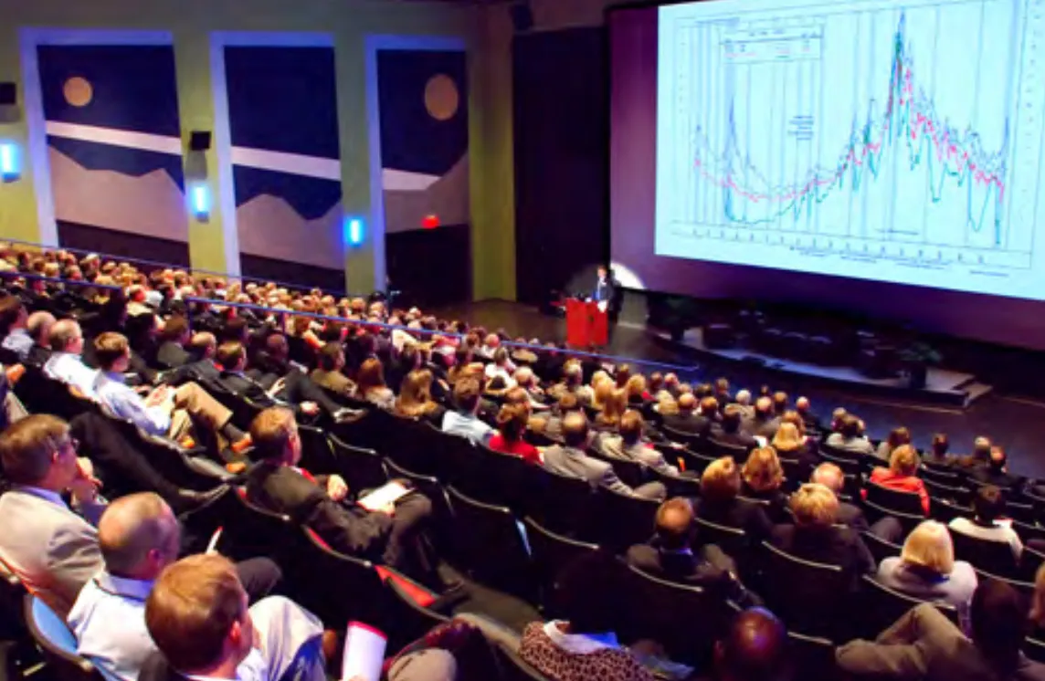 A full audience in the National Geographic Theater facing a speaker and a large data chart on screen